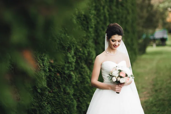 Bela noiva em elegante vestido branco segurando buquê posando no parque — Fotografia de Stock