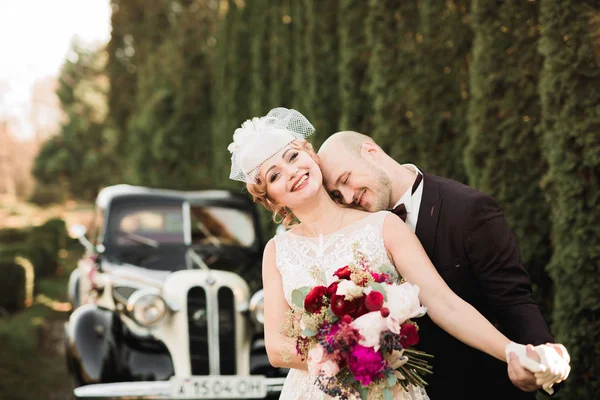 Heureux couple nouvellement marié, homme et femme embrasser près de voiture rétro élégant — Photo