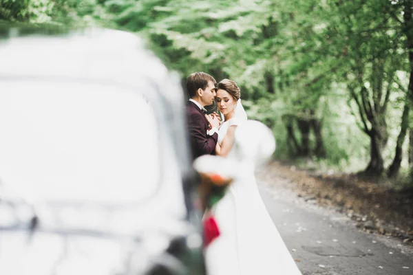 Feliz casal recém-casado, homem e mulher beijando perto de carro retro elegante — Fotografia de Stock