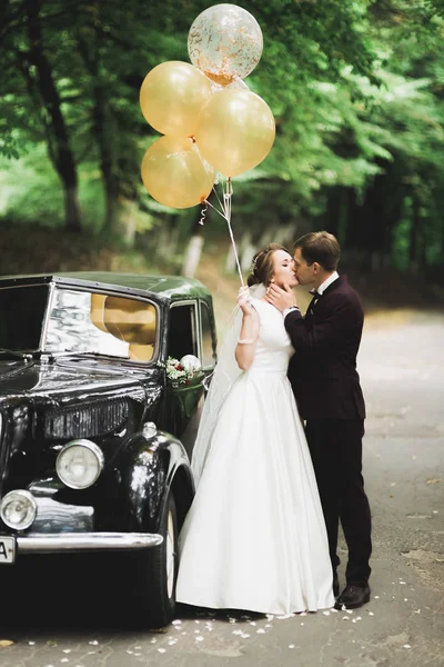 Feliz casal recém-casado, homem e mulher beijando perto de carro retro elegante — Fotografia de Stock