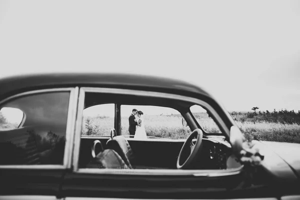 Feliz pareja recién casada, el hombre y la esposa besándose cerca de coche retro con estilo — Foto de Stock