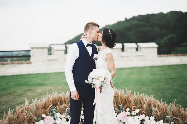 Romantic, fairytale, happy newlywed couple hugging and kissing in a park, trees in background — Stock Photo, Image