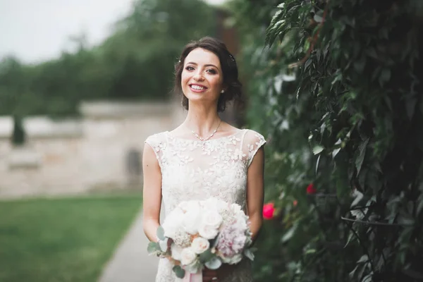 Beautiful brunette bride in elegant white dress holding bouquet posing neat trees — Stock Photo, Image