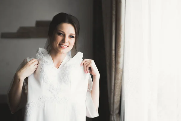 Hermosa novia con vestido de novia de moda con plumas con maquillaje de lujo deleite y peinado, estudio sesión de fotos interior — Foto de Stock