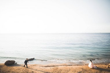 Düğün çifti mavi denizin yanındaki kayalarda öpüşüyor ve sarılıyor.