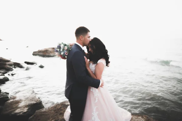 Boda pareja besándose y abrazándose en rocas cerca de mar azul —  Fotos de Stock