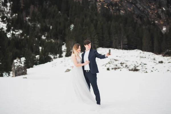 Joven pareja feliz haciendo una selfie, montañas paisaje en la nieve en el fondo —  Fotos de Stock