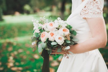 Gelin çiçekli büyük ve güzel bir düğün buketi tutuyor.