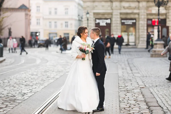 Wedding photo shooting. Bride and bridegroom walking in the city. Married couple embracing and looking at each other. Holding bouquet — Stock Photo, Image