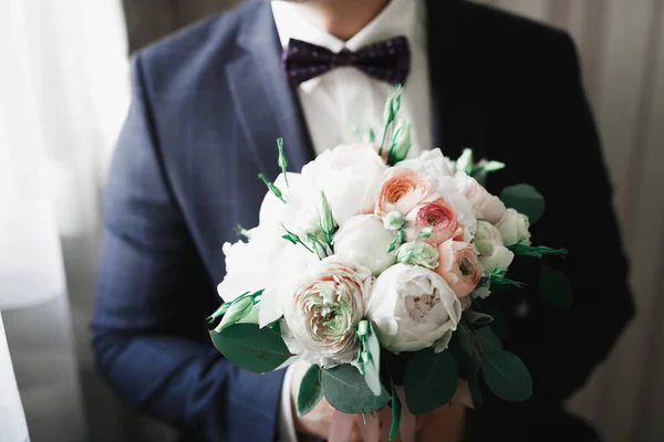 Beautiful man, groom holding big and beautiful wedding bouquet with flowers