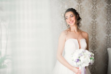 Cüppeli muhteşem gelin bir odada düğün töreni için poz veriyor ve hazırlanıyor.