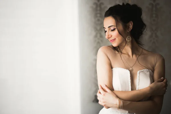 Preciosa novia en bata posando y preparándose para la ceremonia de boda cara en una habitación — Foto de Stock