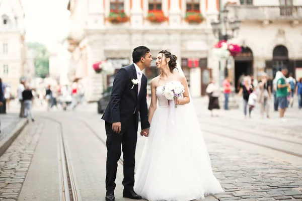 Sesión de fotos de boda. Novia y novio caminando por la ciudad. Pareja casada abrazándose y mirándose. Ramo de celebración — Foto de Stock