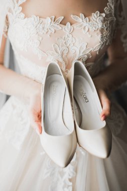 Zarif beyaz elbiseli güzel gelin ellerinde düğün ayakkabıları tutuyor.