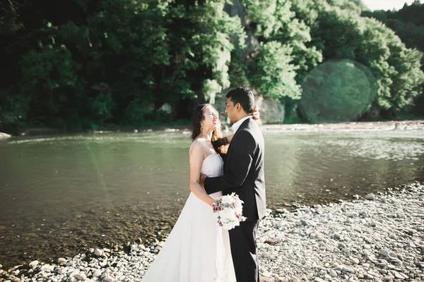 Elegante stijlvolle vrolijke blonde bruid en prachtige bruidegom op de achtergrond van een prachtige rivier in de bergen — Stockfoto