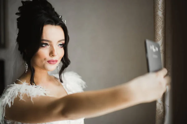 Egy édes mosolygós menyasszony egy világos belső térben szelfit készít a telefonban. — Stock Fotó