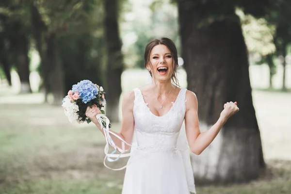 Belle mariée en élégante robe blanche tenant bouquet posant dans le parc — Photo