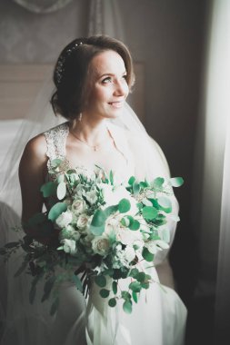 Cüppeli muhteşem gelin bir odada düğün töreni için poz veriyor ve hazırlanıyor.