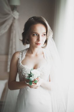 Cüppeli muhteşem gelin bir odada düğün töreni için poz veriyor ve hazırlanıyor.