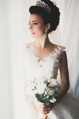 Cüppeli muhteşem gelin bir odada düğün töreni için poz veriyor ve hazırlanıyor.