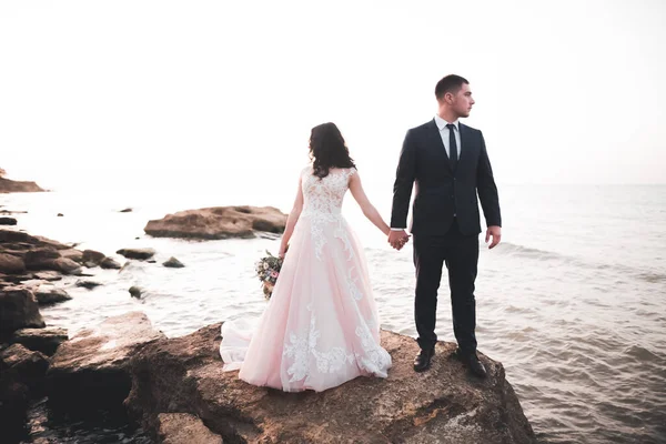 Свадебная пара, жених, невеста с букетом позирует у моря и голубого неба — стоковое фото