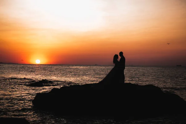 Boda pareja besándose y abrazándose en rocas cerca de mar azul — Foto de Stock