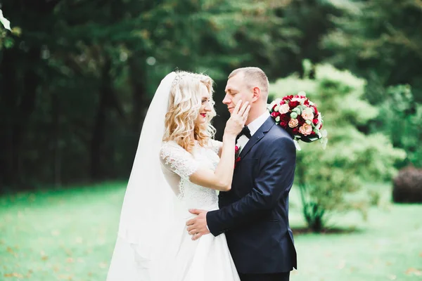 Elegante pareja de recién casados felices caminando en el parque el día de su boda con ramo — Foto de Stock