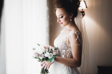 Cüppeli muhteşem gelin bir odada düğün töreni için poz veriyor ve hazırlanıyor.