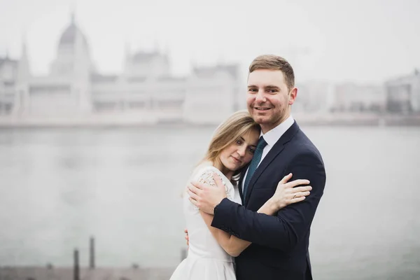 Όμορφη πανέμορφη νύφη που ποζάρει στον γαμπρό και διασκεδάζει, κοντά στο κοινοβούλιο της Βουδαπέστης, χώρος για κείμενο, ζευγάρι γάμου — Φωτογραφία Αρχείου