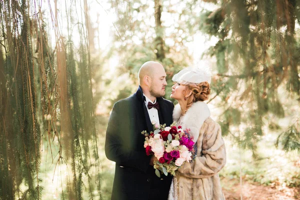 Elegante coppia di sposi felici che passeggiano nel parco il giorno del loro matrimonio con bouquet — Foto Stock