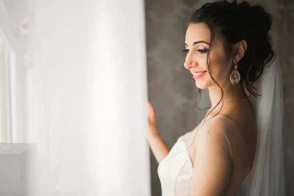 Preciosa novia en bata posando y preparándose para la ceremonia de boda cara en una habitación —  Fotos de Stock