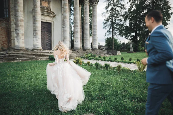 Elegante coppia di sposi felici. Sposa in esecuzione da sposo nel parco il giorno del loro matrimonio — Foto Stock