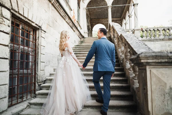 Hermosa pareja de boda subiendo una hermosa escalera tomados de la mano y se mira entre sí — Foto de Stock