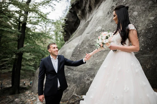 Piękna piękna panna młoda pozowanie do pana młodego i zabawy w pobliżu w górach z niesamowitym widokiem, miejsce na tekst, para ślubna — Zdjęcie stockowe