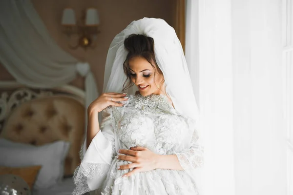 Preciosa novia en bata posando y preparándose para la ceremonia de boda cara en una habitación —  Fotos de Stock