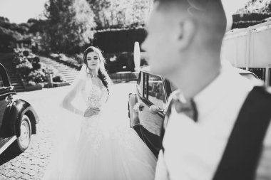 Gelin ve damat, zarif bir çift retro düğün arabasının yanında kalıyor.