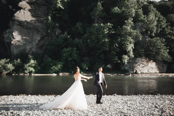 Elegante novia rubia feliz y elegante novio en el fondo de un hermoso río en las montañas —  Fotos de Stock