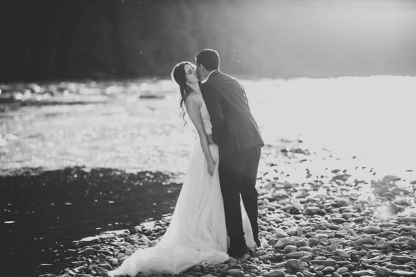 Elegante novia rubia feliz y elegante novio en el fondo de un hermoso río en las montañas —  Fotos de Stock