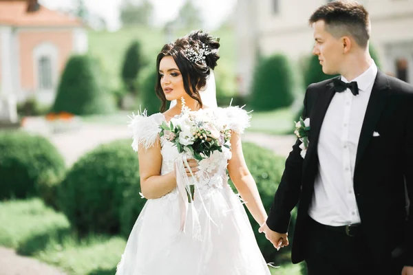 Stilvolles Brautpaar spaziert am Hochzeitstag mit Blumenstrauß durch den Park — Stockfoto