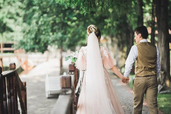 結婚式の日に公園を歩く幸せな新婚旅行のスタイリッシュなカップル花束 — ストック写真