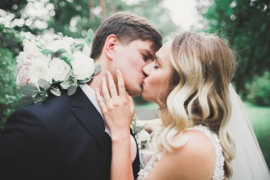 Romantik, peri masalı, mutlu yeni evli çift parkta sarılıp öpüşüyor, arka planda ağaçlar...