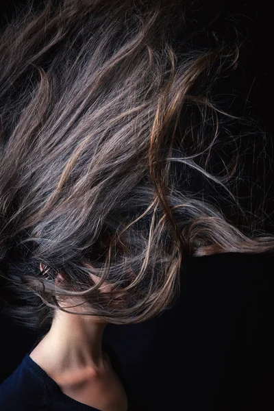 Girl throwing hair in the air on black background. Concept image for bad hair day