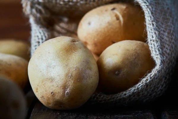 Ahşap arka plan üzerinde taze çiğ patates çuvalı çuval bezi