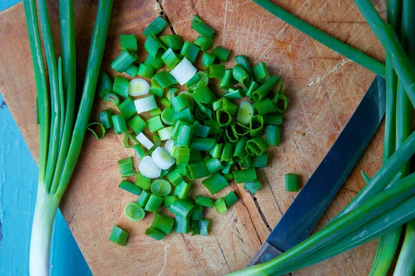 Scallions, also known as green onions, spring onions, or salad onions on rustic chopping board