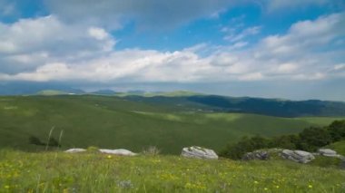 Bu video, çok güzel bir dağ manzarasının zaman atlamasını gösteriyor. Mavi gökyüzünün altında hareket eden dağ sıralarının ve kara bulutların alçak açılı bir görüntüsünü içeriyor.