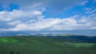 Bu video, çok güzel bir dağ manzarasının zaman atlamasını gösteriyor. Mavi gökyüzünün altında hareket eden dağ sıralarının ve kara bulutların alçak açılı bir görüntüsünü içeriyor.