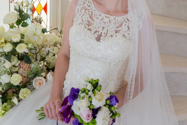 Die Braut sitzt in einem Brautkleid mit einem Strauß in der Hand — Stockfoto