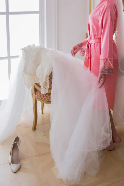 Noiva em um roupão de banho perto de seu vestido de noiva — Fotografia de Stock