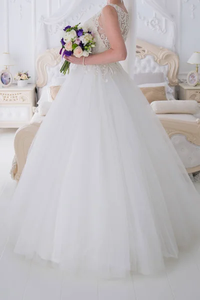 Braut hält einen Hochzeitsstrauß in einem hellen Raum — Stockfoto