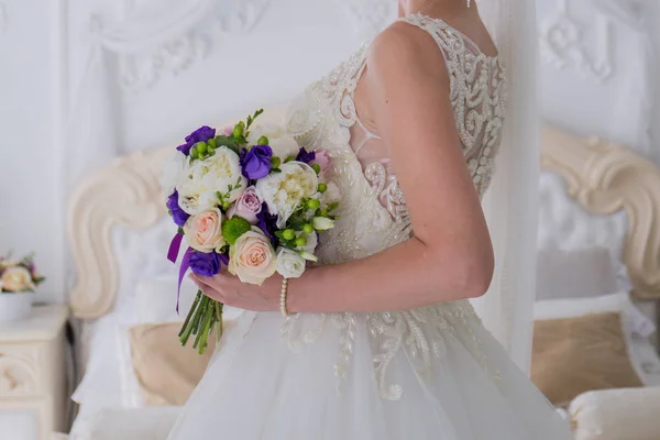 Noiva mantém um buquê de casamento em um quarto brilhante — Fotografia de Stock